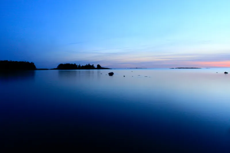 Tyyni meri sinisellä hetkellä, saaret siluettina ja horisontissa vaaleanpunainen juova.